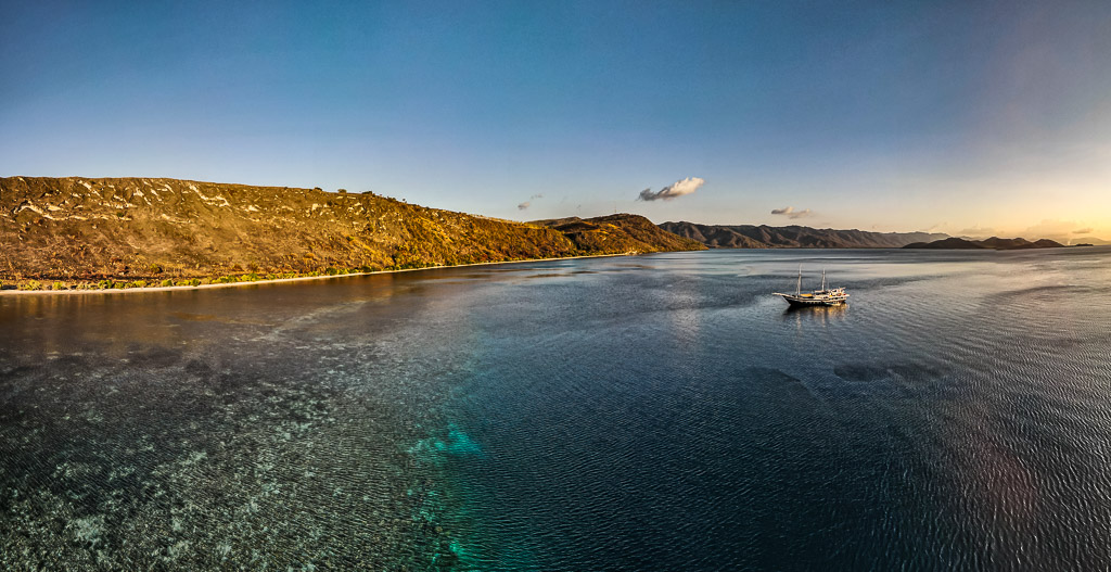 Aerial panorama of a bay with fringing reef and anchored phinisi, Bacatan Wall, Banda Sea, Indonesia