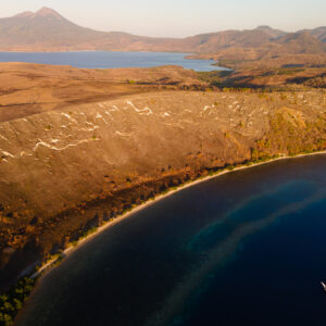 Aerial view of dry coastline, volcano and small phinisi in a bay, Kawula, Banda Sea, Indonesia