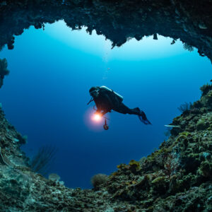 Diver silhouetted in a heart-shaped cave opening with torch, Mike's Delight, Banda Sea, Indonesia