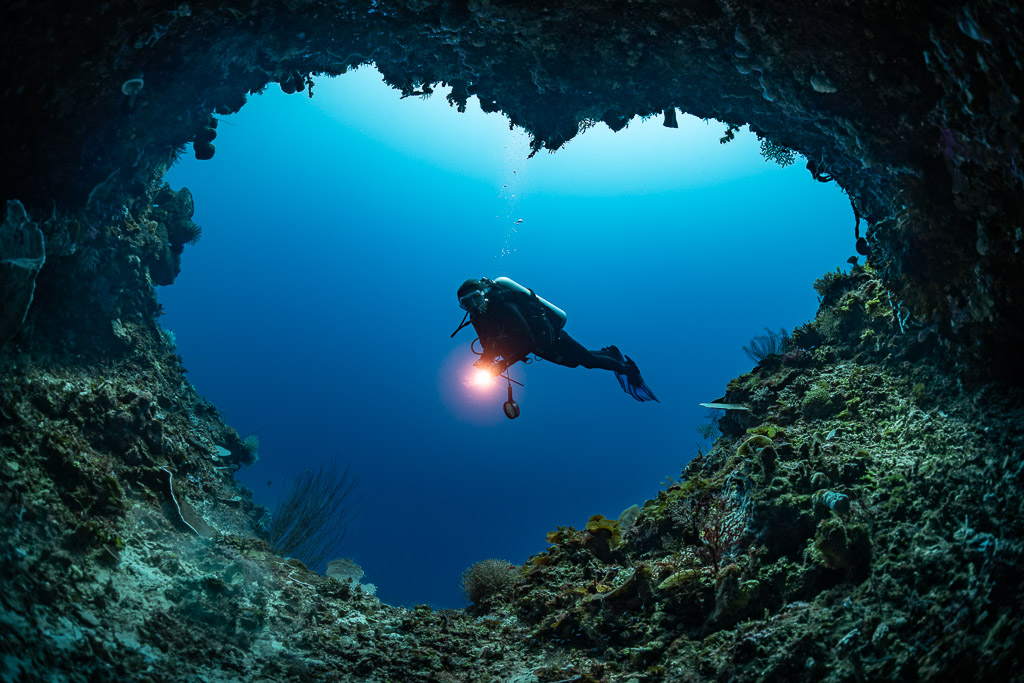 Diver silhouetted in a heart-shaped cave opening with torch, Mike's Delight, Banda Sea, Indonesia