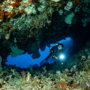 Diver lighting the exit of a reef swim-through, The Arch, Banda Sea, Indonesia