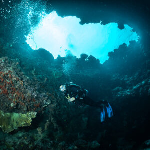 Diver inside an underwater cave below a bright opening, Hole in the Wall, Banda Sea, Indonesia