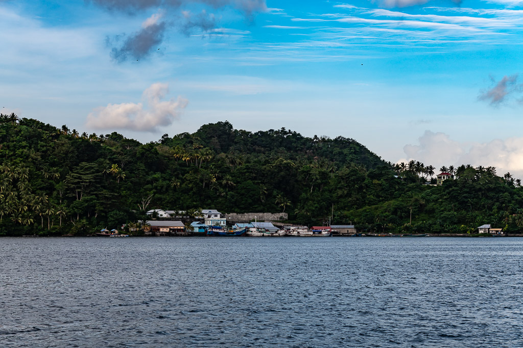 Village côtier au pied de collines boisées sous un ciel bleu, îles Banda, mer de Banda, Indonésie