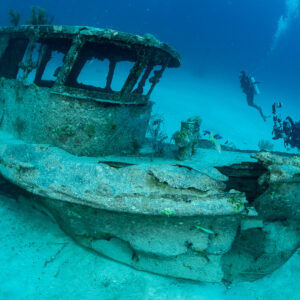 Divers exploring the wheelhouse of a small boat wreck on sand, Grand Bahama, Bahamas