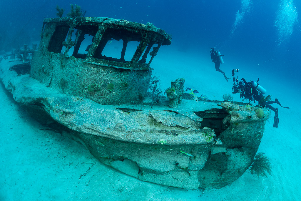 Divers exploring the wheelhouse of a small boat wreck on sand, Grand Bahama, Bahamas