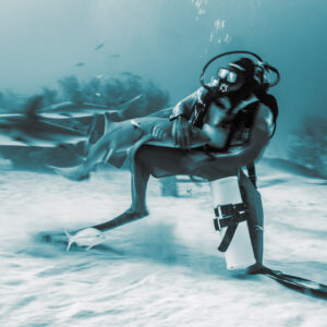 Cyan-toned monochrome, feeder with a shark across his lap, blurred sharks behind, Shark Junction, Grand Bahama, Bahamas
