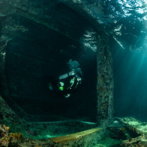 Diver framed by encrusted concrete wreck interior arches, SS Sapona wreck, Bimini, Bahamas