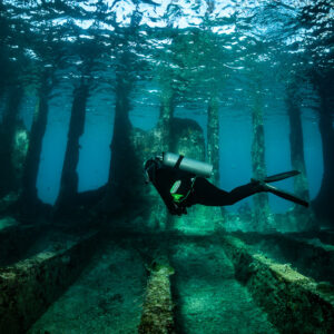 Diver swimming over wreck floor beams under rippled surface, SS Sapona wreck, Bimini, Bahamas