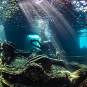 Diver inside a wreck seen through a porthole frame, sunbeams streaming down, SS Sapona wreck, Bimini, Bahamas