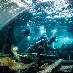 Three divers swimming through a wreck interior pierced by sunbeams, SS Sapona wreck, Bimini, Bahamas