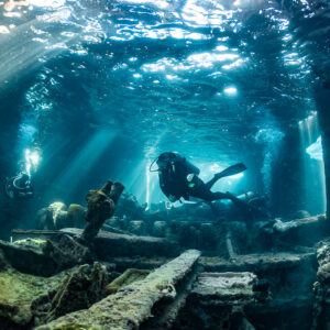 Diver swimming above wreck debris under a broken deck and light rays, SS Sapona wreck, Bimini, Bahamas