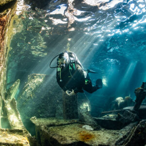 Diver hovering beside an encrusted wall inside a sunlit wreck, SS Sapona wreck, Bimini, Bahamas