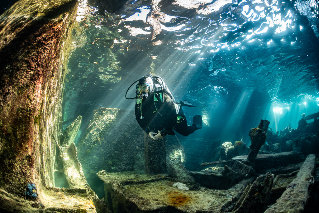 Diver hovering beside an encrusted wall inside a sunlit wreck, SS Sapona wreck, Bimini, Bahamas