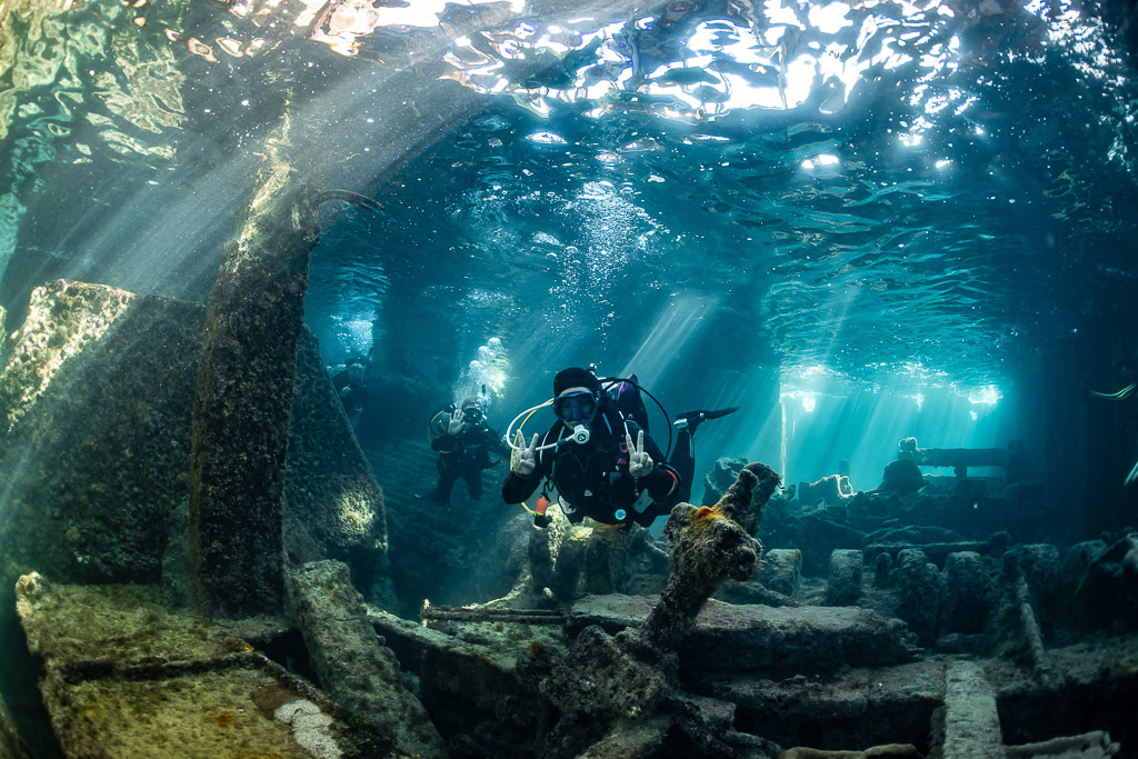 Diver with camera facing the lens among wreck beams and sunbeams, SS Sapona wreck, Bimini, Bahamas