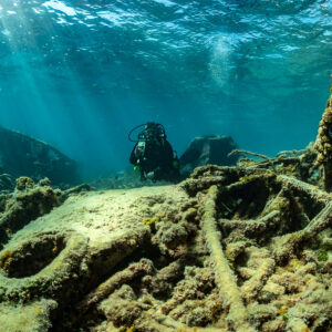 Diver beyond scattered wreck debris and cables in shallow water, SS Sapona wreck, Bimini, Bahamas