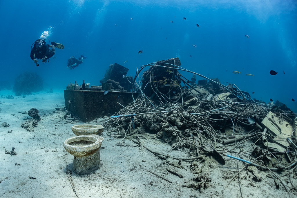 Diver above a tangle of cables and toilet bowls on a broken wreck, Shaab Marsa Alam, Red Sea, Egypt