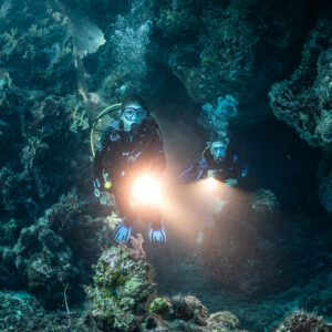 Two divers with torches lighting a dark reef cavern, Zabargad, Red Sea, Egypt