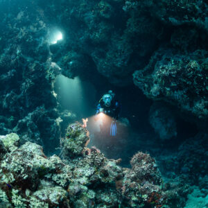 Diver with torch emerging from a reef cave under light from above, Zabargad, Red Sea, Egypt
