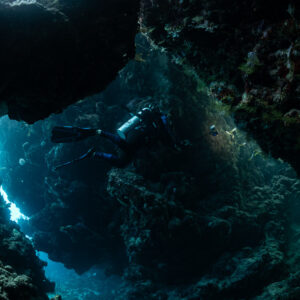 Diver swimming through a dark cave with bright openings behind, Zabargad, Red Sea, Egypt