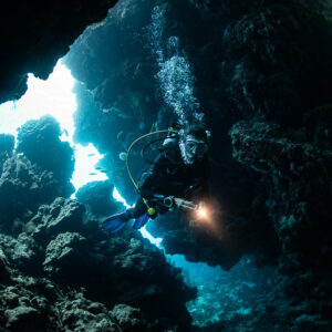 Diver with torch in a cave entrance backlit by blue light, Zabargad, Red Sea, Egypt