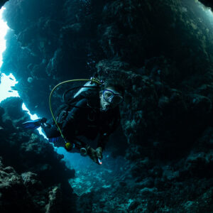 Diver turning inside a dark cave beside a blue opening, Zabargad, Red Sea, Egypt