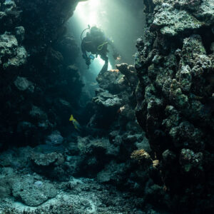 Diver in a sunlit cave passage with light beams from above, Zabargad, Red Sea, Egypt