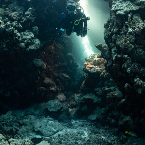Diver entering a cave passage lit by a bright shaft of light, Zabargad, Red Sea, Egypt