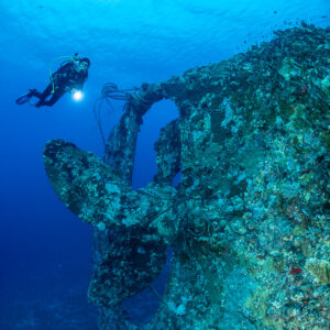 Diver with torch beside an overgrown wreck propeller in deep blue, Levanzo wreck, Red Sea, Egypt