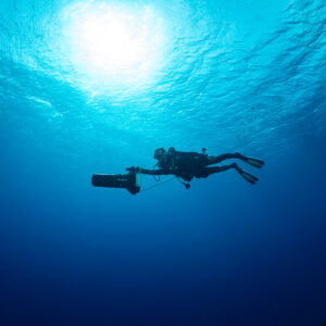 Diver with scooter silhouetted against the sun in open blue water, Levanzo wreck, Red Sea, Egypt