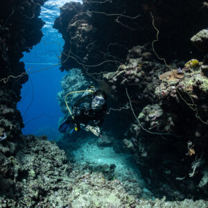 Diver entering a narrow rock passage, vertical, Gota Elba, Red Sea, Egypt