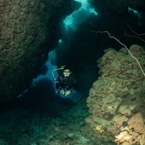 Diver crossing a narrow sunlit fissure between rocks, Gota Elba, Red Sea, Egypt