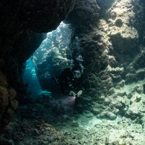 Diver in a dark arch opening onto blue water, Gota Elba, Red Sea, Egypt