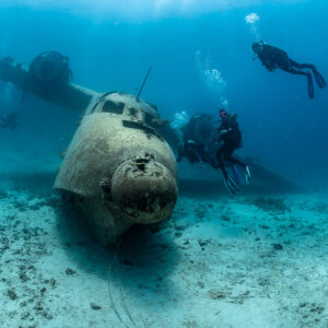 Divers gathered beside the nose of a seaplane wreck on sand, Grumman HU-16 Albatross wreck, Red Sea, Egypt