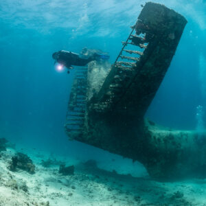 Diver with torch facing the upright tail of a seaplane wreck, vertical, Grumman HU-16 Albatross wreck, Red Sea, Egypt
