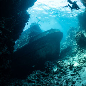 Diver above a wreck hull resting against a reef wall, vertical, Sabri Baba 1 wreck, Red Sea, Egypt
