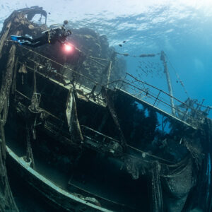 Diver with torch on a wreck draped with old fishing nets, Sabri Baba 1 wreck, Red Sea, Egypt