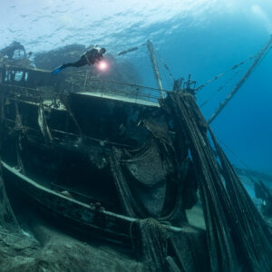 Diver with torch above the net-covered superstructure of a wreck, Sabri Baba 1 wreck, Red Sea, Egypt