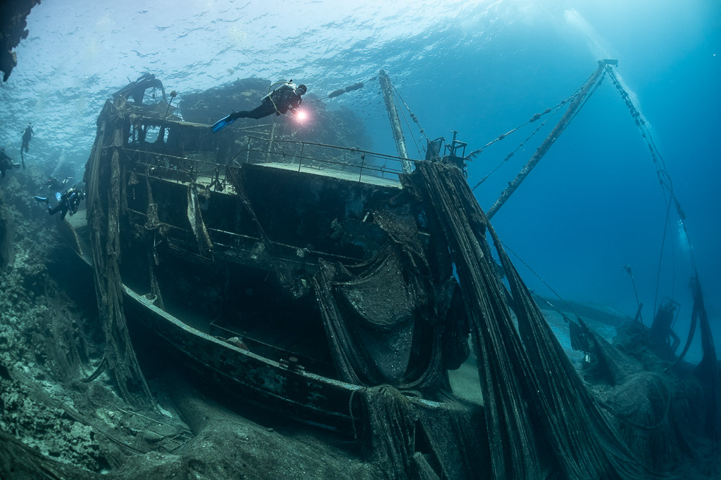 Diver with torch above the net-covered superstructure of a wreck, Sabri Baba 1 wreck, Red Sea, Egypt