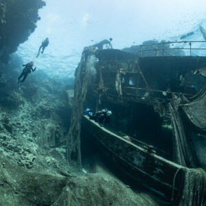 Divers around a net-draped wreck lying beside a reef wall, Sabri Baba 1 wreck, Red Sea, Egypt
