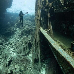 Diver beside the hull of a wreck against a reef wall, vertical, Sabri Baba 1 wreck, Red Sea, Egypt
