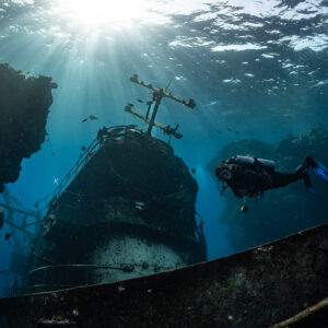 Diver passing the mast of a wreck under sun rays, Sabri Baba 1 wreck, Red Sea, Egypt