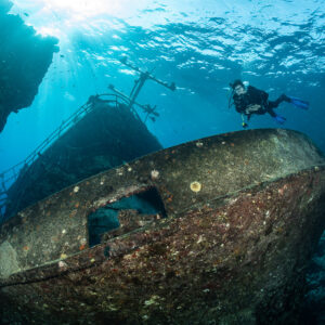 Diver above the rusty bow of a wreck between reef walls, Sabri Baba 1 wreck, Red Sea, Egypt