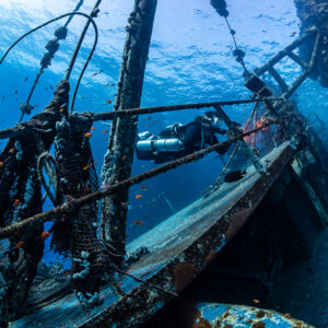 Diver among net-draped masts and rigging on a wreck deck, Sabri Baba 1 wreck, Red Sea, Egypt