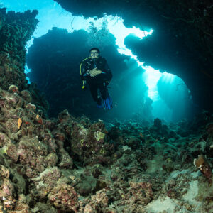 Diver framed in cave opening with light streaming in, vertical, Gota Abu Fendira, Red Sea, Egypt