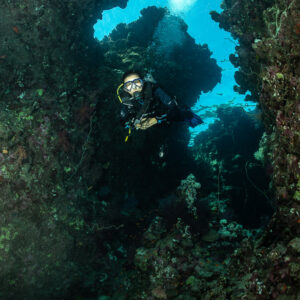 Diver in narrow reef crevice with blue light above, vertical, Gota Abu Fendira, Red Sea, Egypt