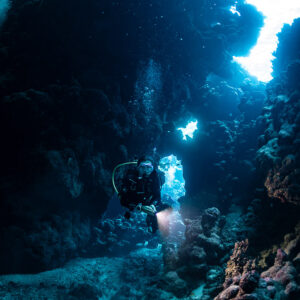 Diver with torch in cave beneath bright opening, vertical, Shaab Claudio, Red Sea, Egypt