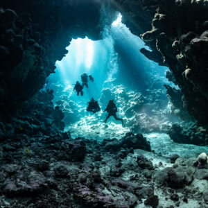Group of divers entering sunlit cave chamber, Shaab Claudio, Red Sea, Egypt