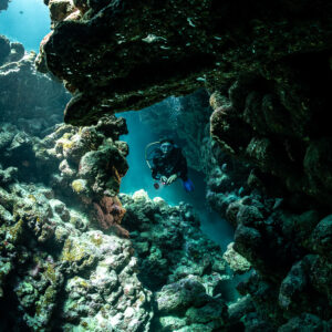 Diver in cave passage under rock overhang, Shaab Claudio, Red Sea, Egypt
