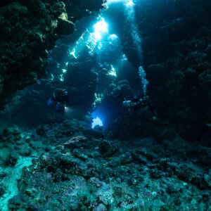 Divers with torches in sunlit cave with light shafts, Shaab Claudio, Red Sea, Egypt