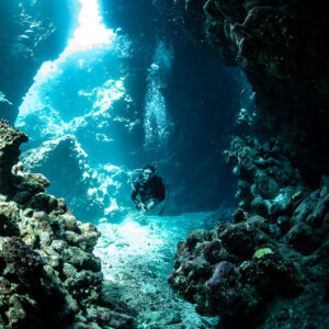 Diver in sunlit cave corridor between rock walls, vertical, Shaab Claudio, Red Sea, Egypt